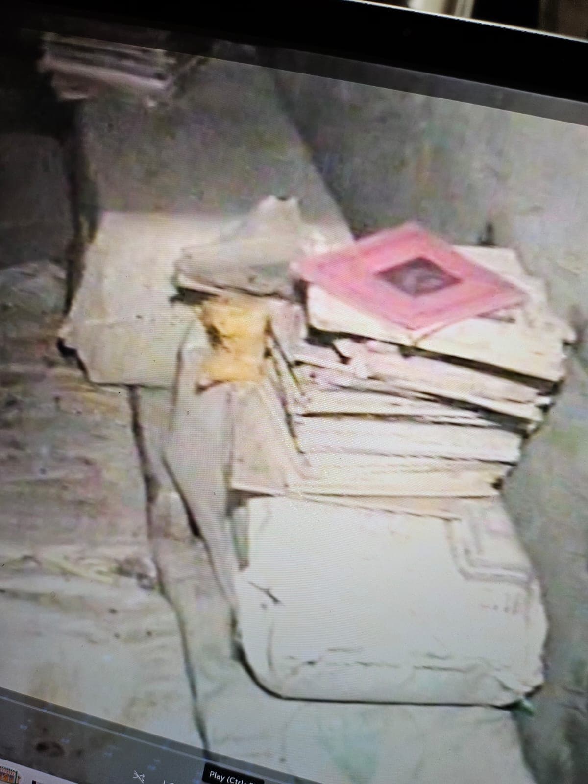A stack of old handwritten notebooks tied together, a pink-covered notebook with a small framed photo on top, on a dusty stone surface